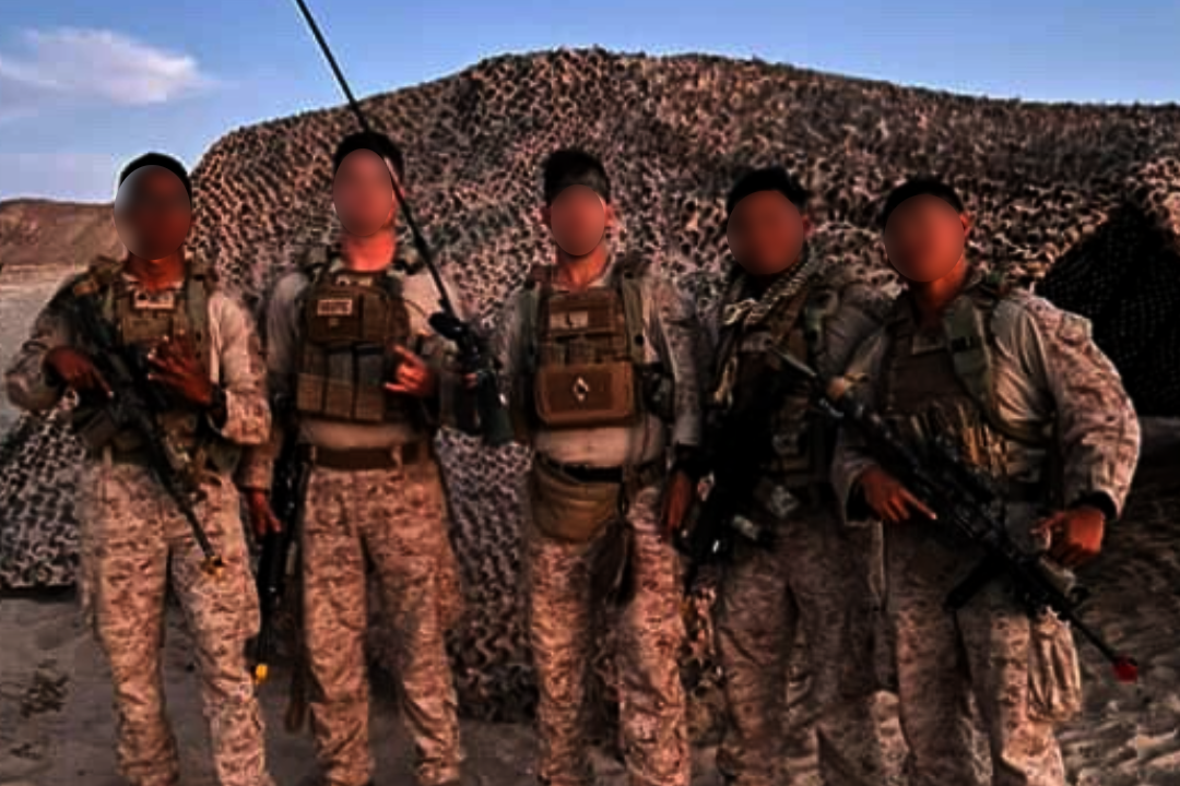Group of soldiers in camouflage uniforms standing in a desert landscape.